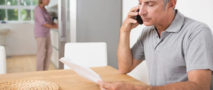 elderly man sitting at a table on the phone holding a piece of paper