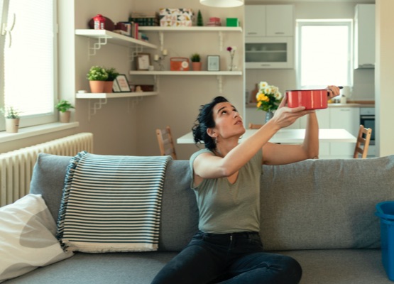 Shocked Woman Looks at the Ceiling While Collecting Water Which Leaks in the Living Room at Home. Worried Woman Holding Bucket While Water Droplets Leak From Ceiling in Living Room