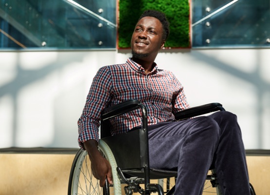 African man in wheelchair looking away and smiling at modern office