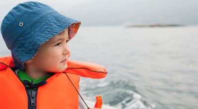 toddler in blue hat and bright orange life jacket on a boat