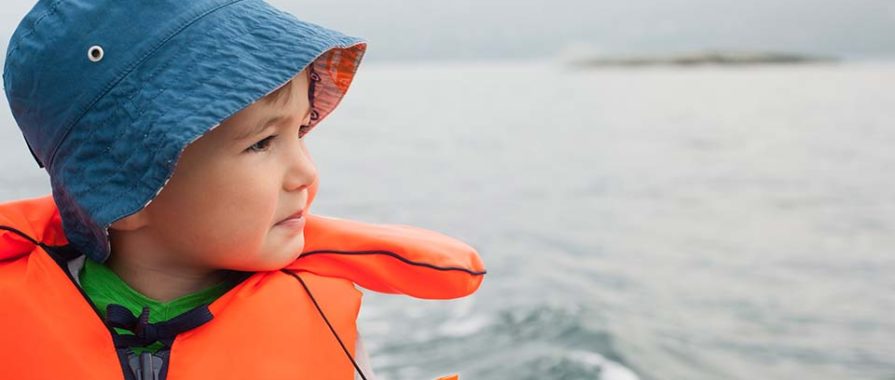 toddler in blue hat and bright orange life jacket on a boat